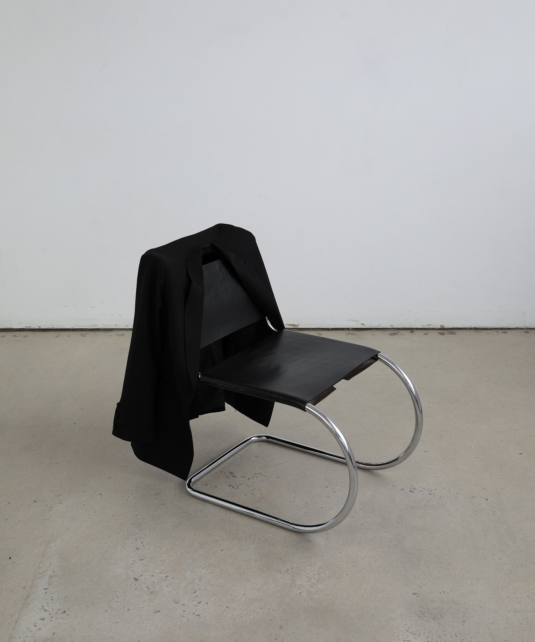 Studio set up with a vintage black leather chair with silver curved legs and a minimalist black tailored blazer hanging over the back of the chair
