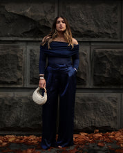 Woman in a navy blue outfit holding a textured handbag against a stone wall.