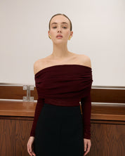 Woman wearing a burgundy off-shoulder top and black skirt against a neutral background