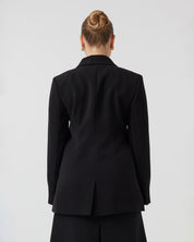 Youthful woman with pulled back dark blonde hair, with a curvaceous figure, photographed from the back wearing tailored black blazer