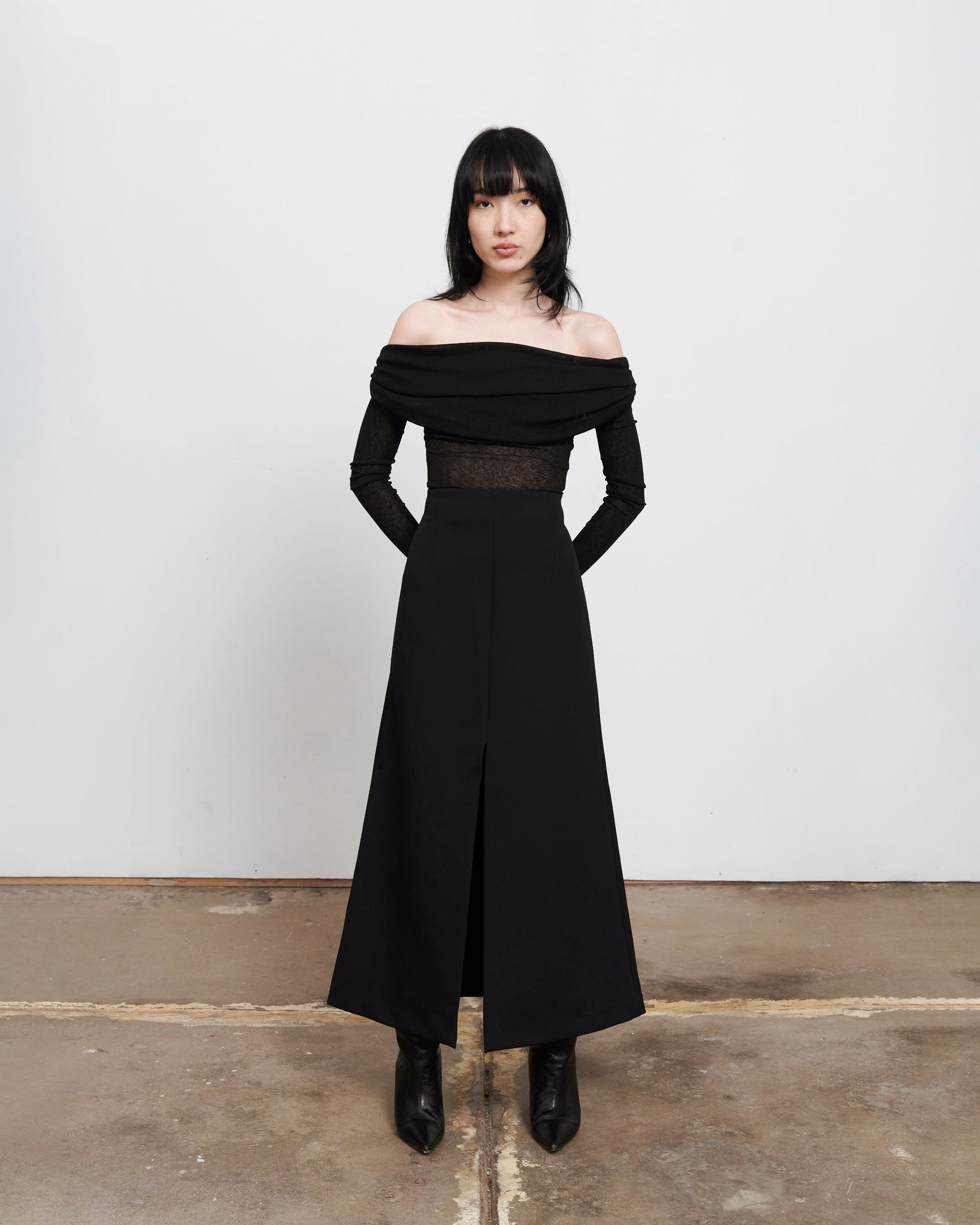 Full body image of The Ada Top, a Black semi sheer, rouched off the shoulder top on women with dark hair and hands gently placed behind her back