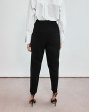 Back view of minimalistic high-waisted black peg leg trousers on a middle aged woman.