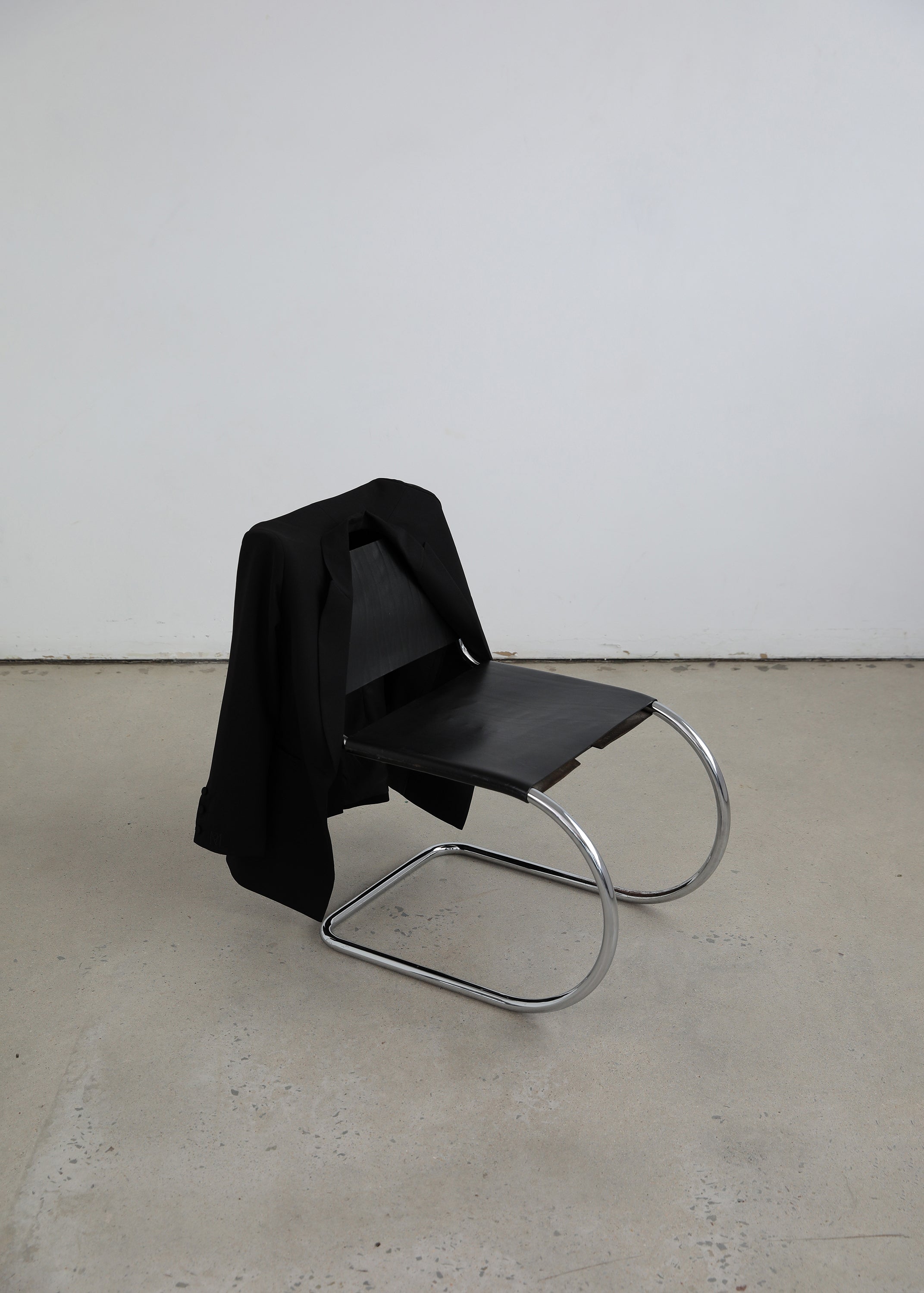 Studio set up with a vintage black leather chair with silver curved legs and a minimalist black tailored blazer hanging over the back of the chair