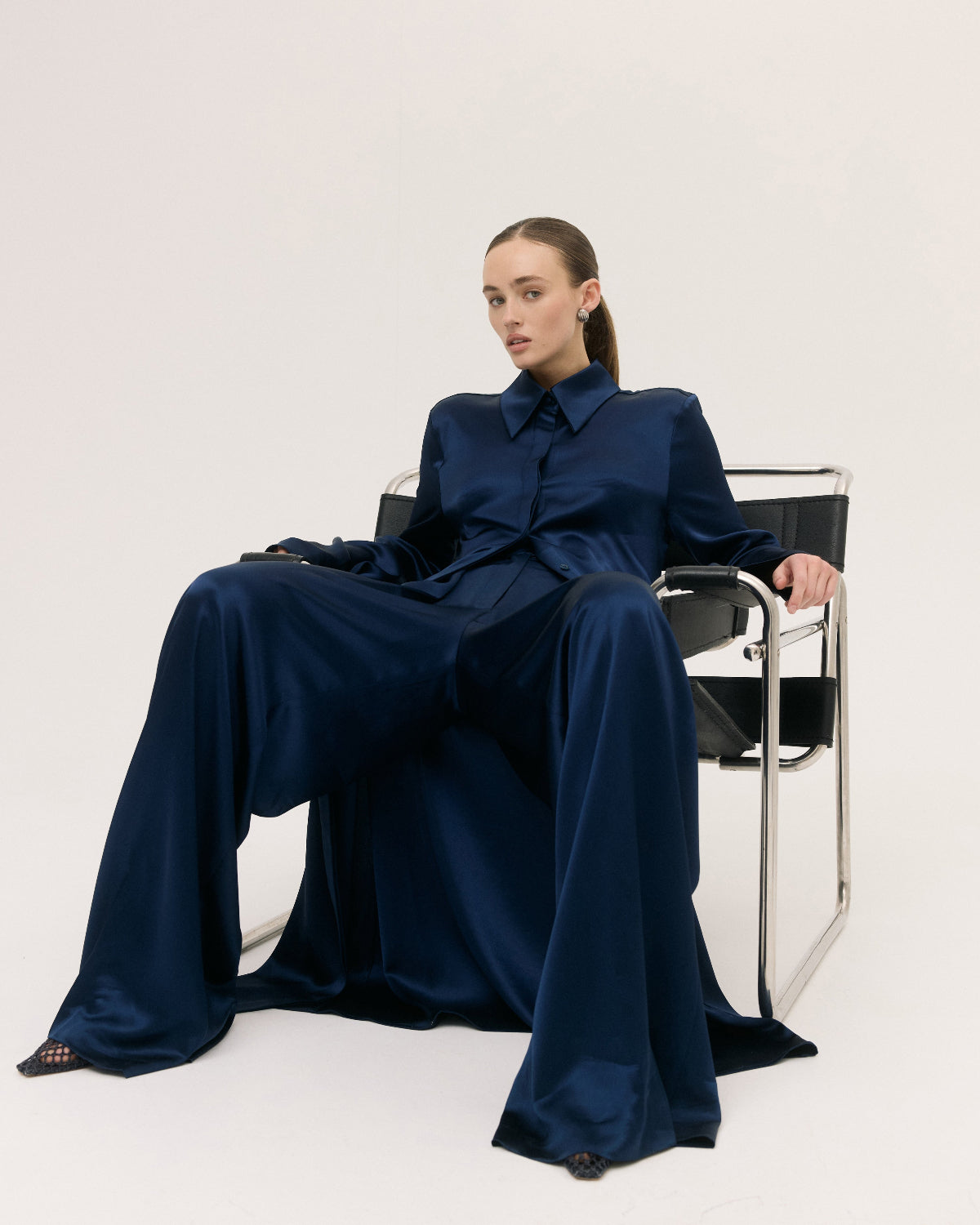 Woman in a navy blue dress sitting on a chair against a white background