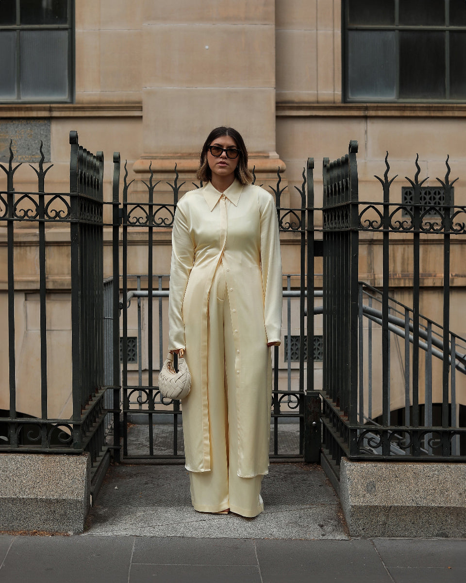 Woman in a light-colored outfit standing in front of a building with black metal gates.