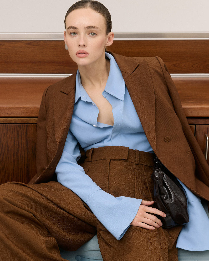 Woman in a brown suit and light blue shirt sitting on a couch.