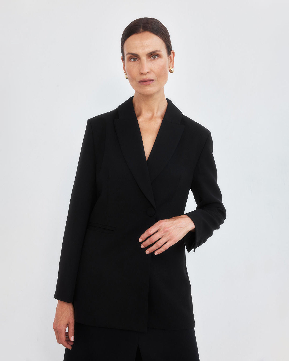 Middle aged women with brown pulled back hair holding the waist of a tailored black blazer