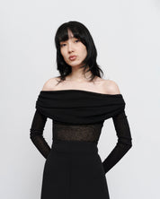 Black semi sheer, rouched off the shoulder top on women with dark hair and hands gently placed behind her back 