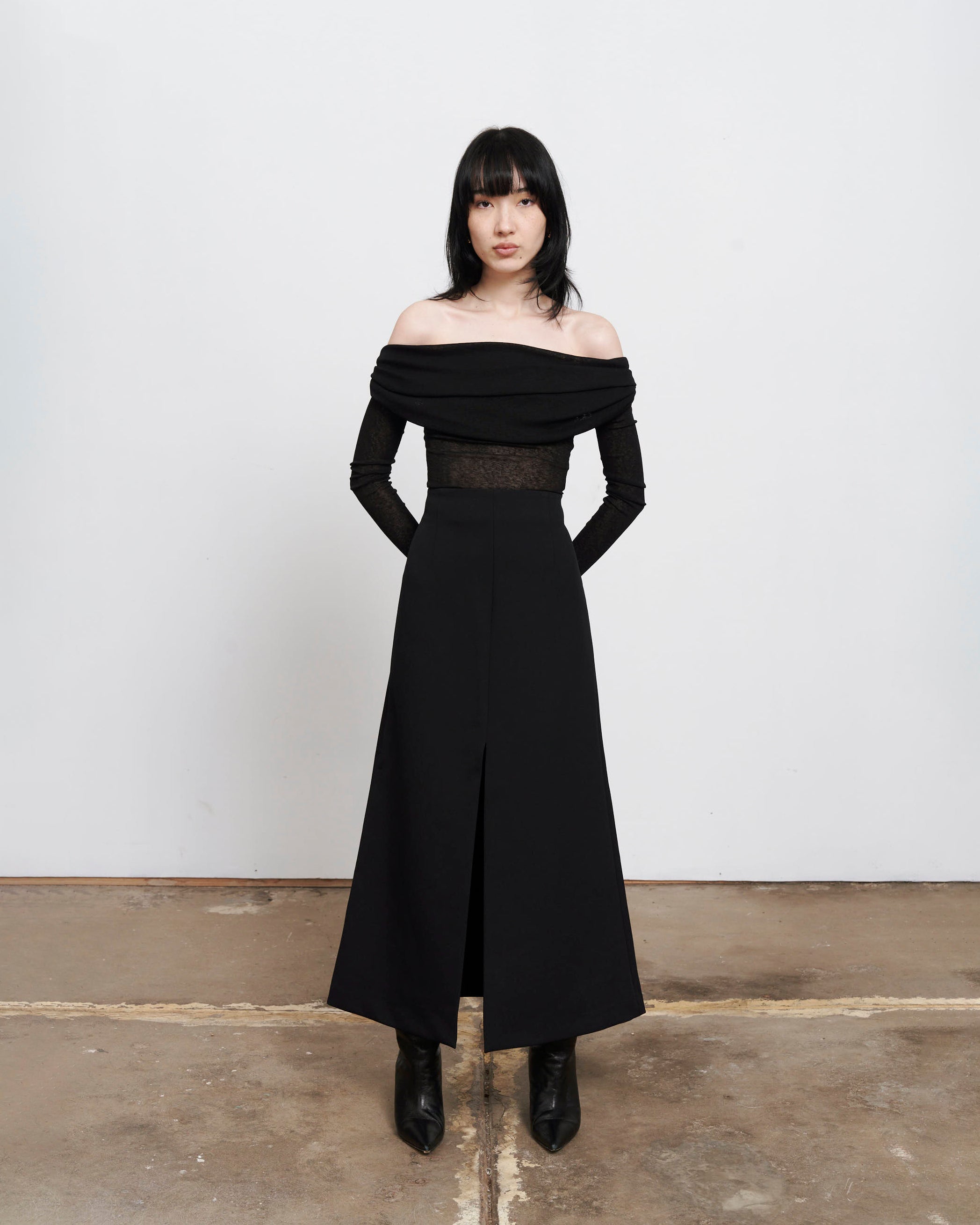 Full body image of The Ada Top, a Black semi sheer, rouched off the shoulder top on women with dark hair and hands gently placed behind her back 