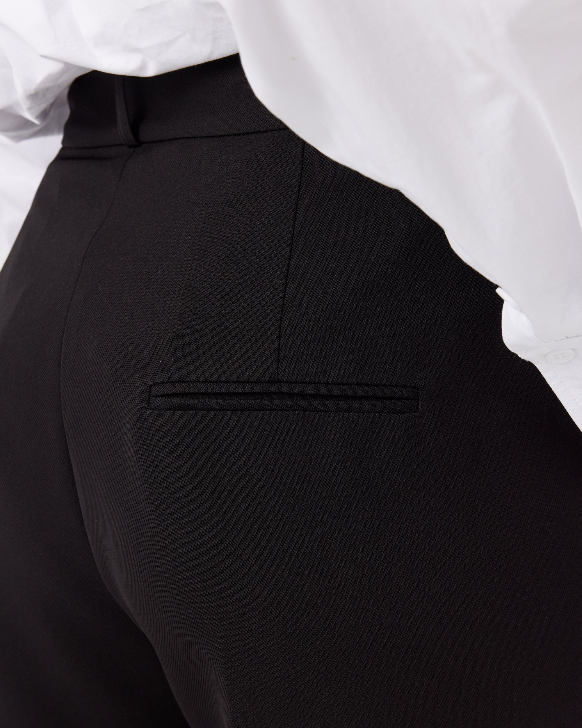 Close up photograph of a curvaceous woman wearing a pair of minimalistic high waisted black wide leg trousers. Photograph shows the back pocket detail of the trousers