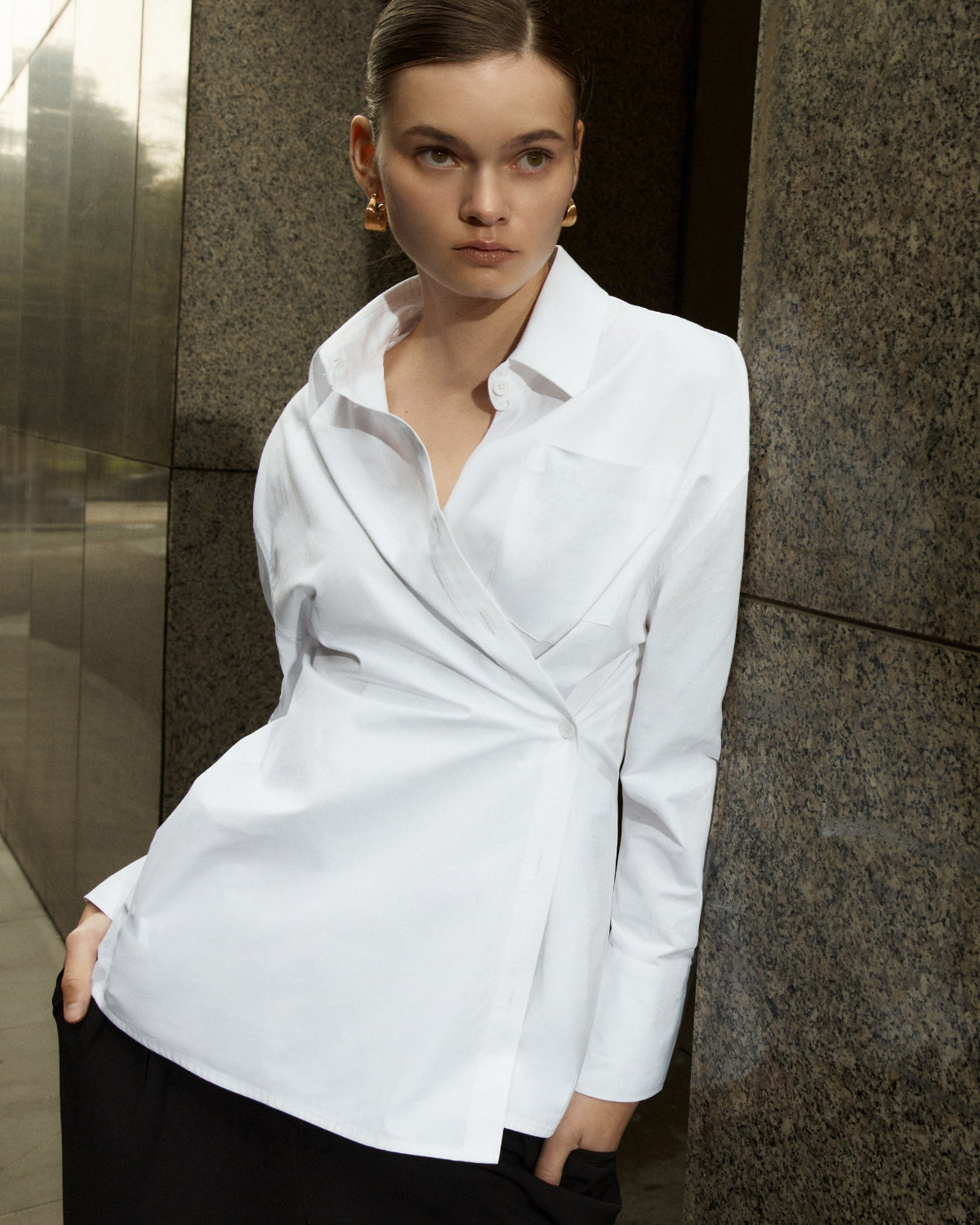 A person wearing a classic white button-down shirt with a wrapped design, featuring a V-neck and side buttons, paired with dark pants.
